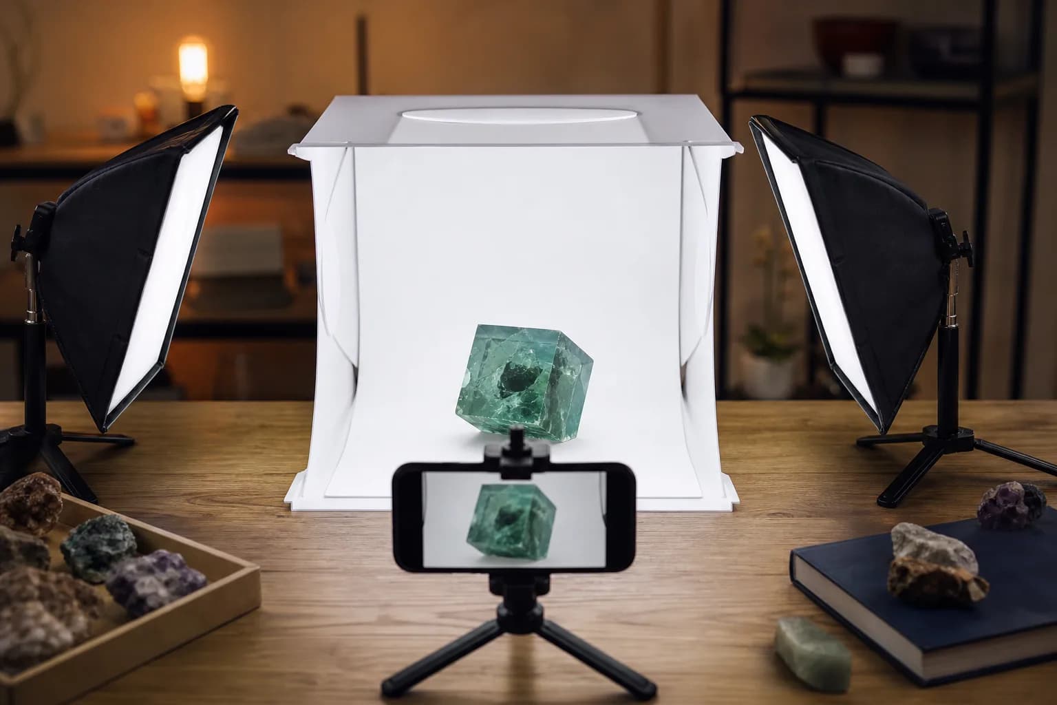 A smartphone on a mini tripod pointed at a fluorite cube inside a white lightbox, with two softbox lights at 45 degree angles